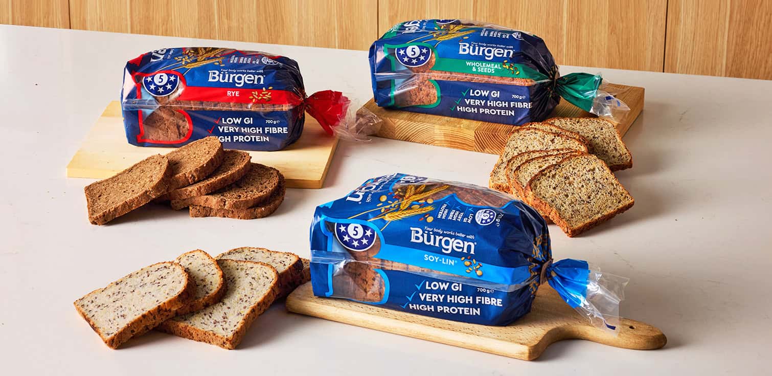 Burgen Rye, Wholemeal and Seeds, and Soy-Lin bread loaves with sliced bread on wooden boards